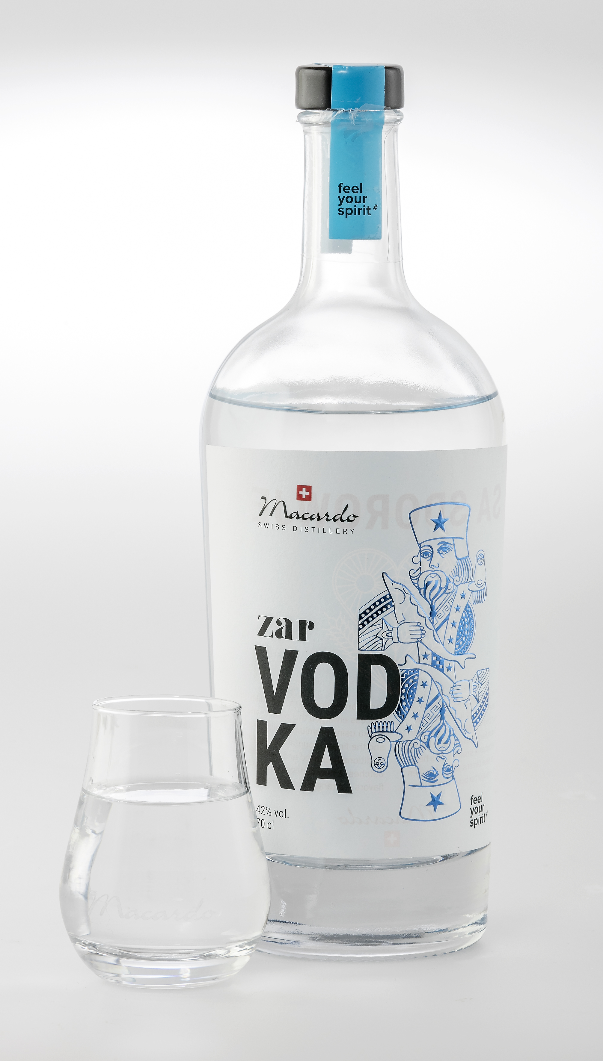 Eine klare Flasche Zar Vodka mit blauem Etikett steht neben einem kleinen Glas gefüllt mit klarer Flüssigkeit, vermutlich Vodka. Auf dem Etikett ist eine stilisierte Figur abgebildet. Flasche und Glas stehen vor einem weißen Hintergrund.
